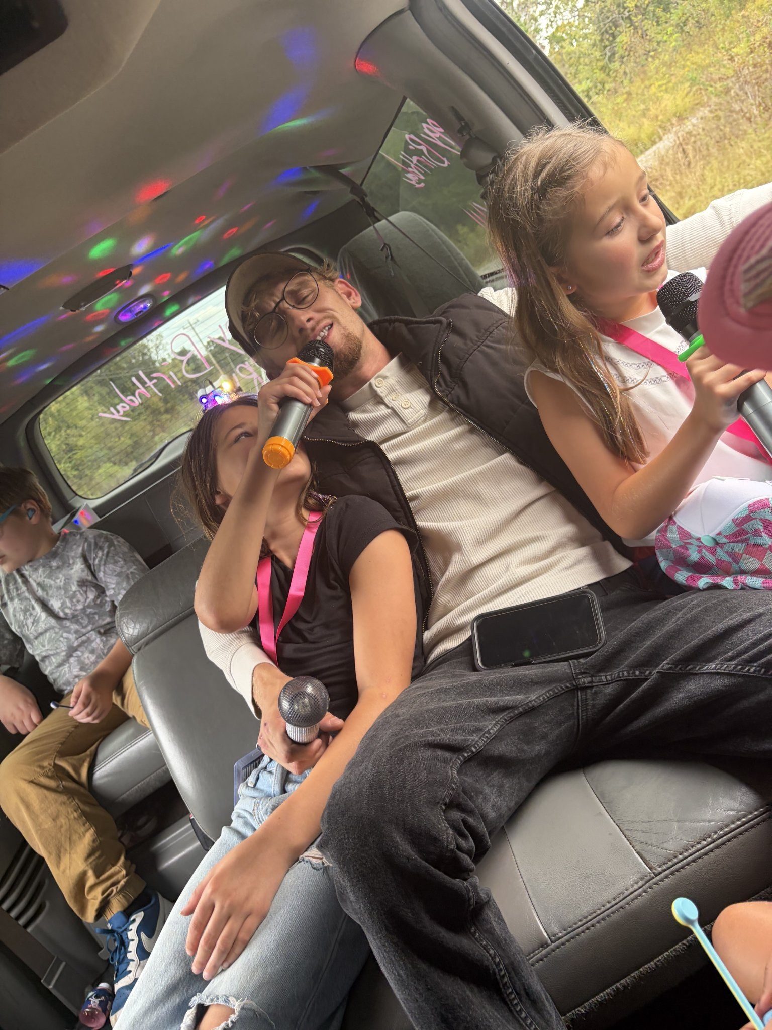 Kids singing karaoke with microphones inside the Nashville party limo under disco party lights at a birthday ride